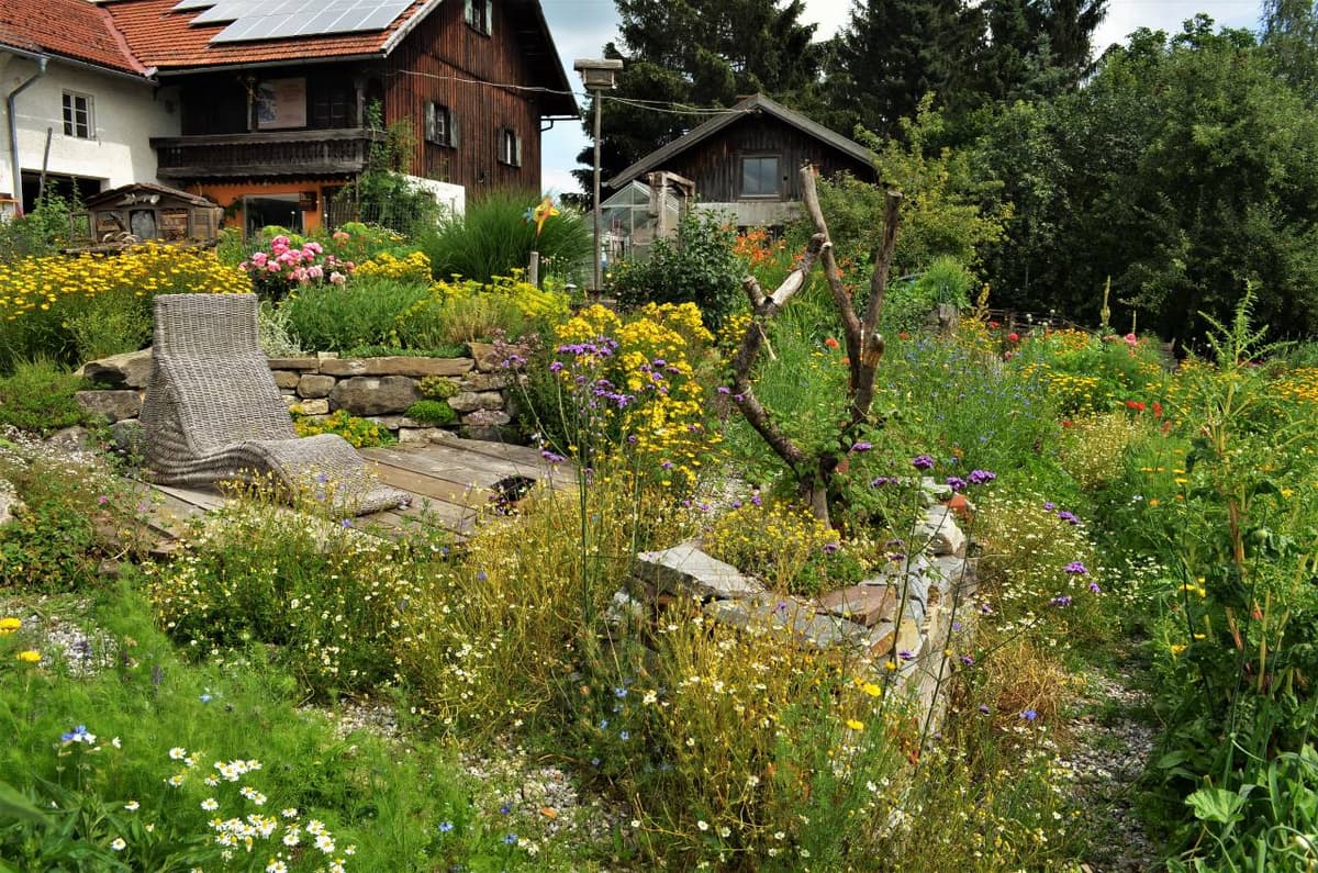 Permakultur-Garten im Allgäu mit blühenden Wildstauden, Natursteinmauer und Sitzplatz